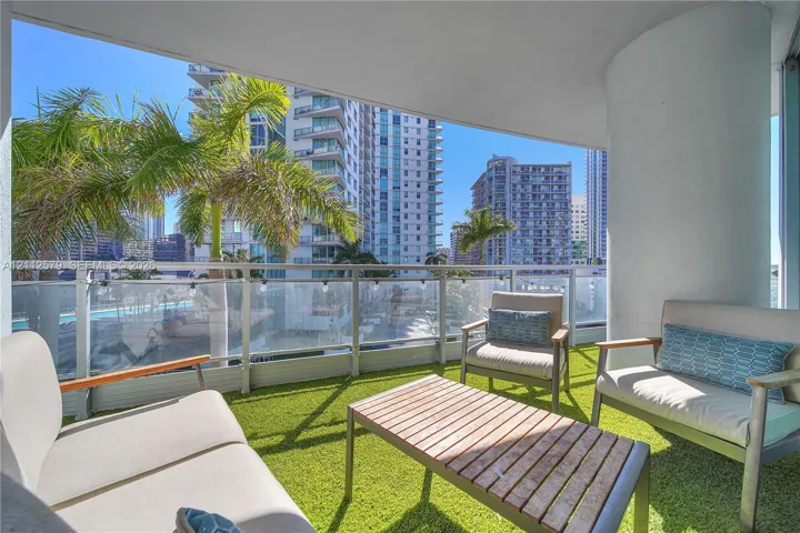 Covered balcony featuring artificial turf flooring, a metal and glass railing system, and a structural concrete column