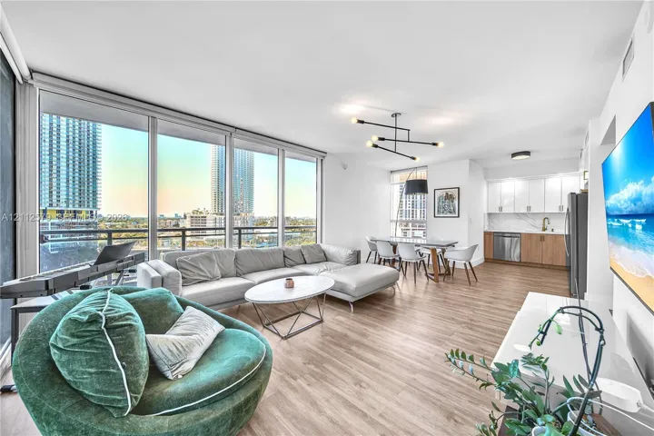 Floor-to-ceiling windows, wood-finish flooring, linear chandelier, minimalist kitchen cabinetry, and stone-finish backsplash