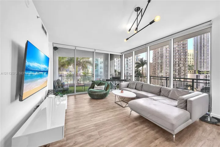 Floor-to-ceiling windows, wood-finish flooring, linear multi-arm light fixture, and an attached balcony with metal railing