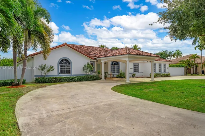 Single-story residence featuring a tile roof, arched windows, a covered porte-cochère, and a circular concrete driveway set on a landscaped lot