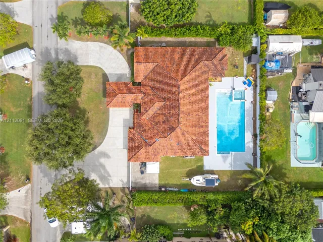 Aerial perspective featuring a tile roof, concrete driveway, and an in-ground pool with a surrounding patio