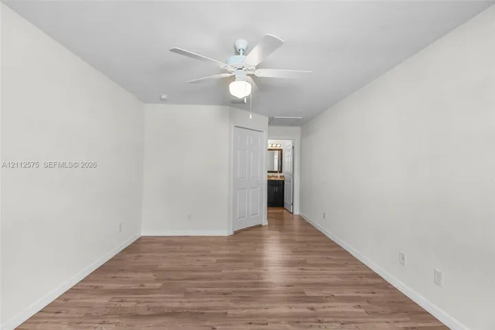 Interior space featuring wood-finish flooring, white walls, and a ceiling fan with integrated lighting
