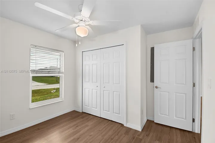 Wood-finish flooring, white paneled interior doors, double-door closet, neutral wall paint, and overhead ceiling fan with integrated lighting