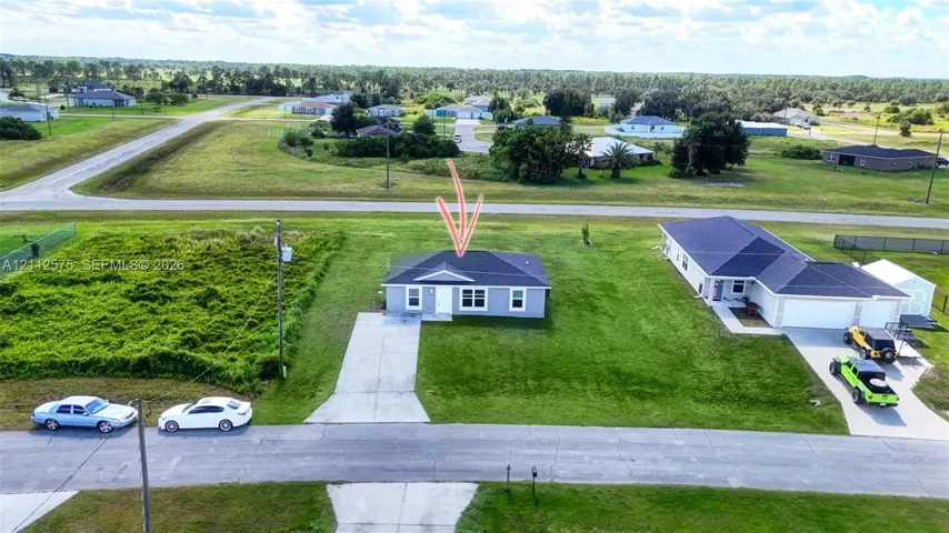 Single-story residence featuring a hipped roof, light-toned exterior siding, and an expansive lot with a paved driveway