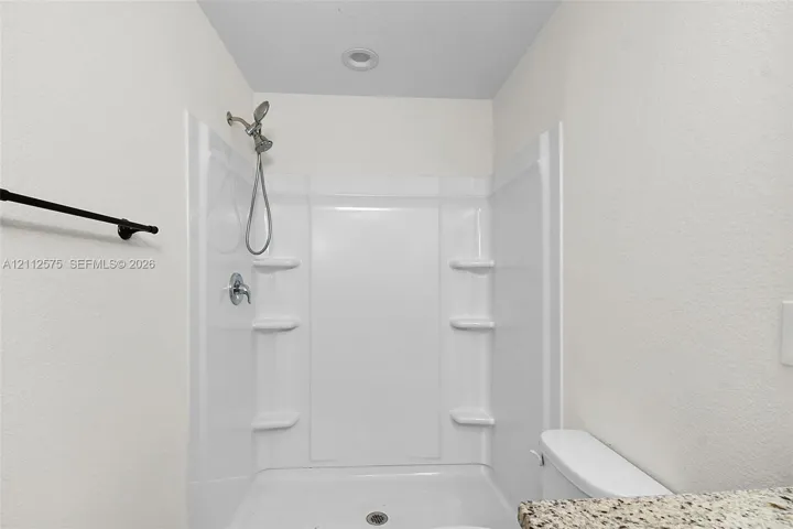 Walk-in shower enclosure with integrated shelving, handheld showerhead, recessed ceiling lighting, and a stone-finish countertop