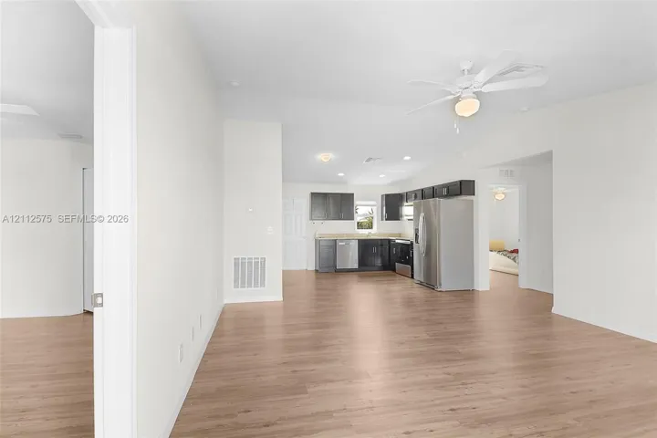 Open-concept interior featuring light wood-finish flooring, vaulted ceilings with a mounted paddle fan, and a kitchen equipped with dark-toned cabinetry, light-colored countertops, and stainless steel appliances