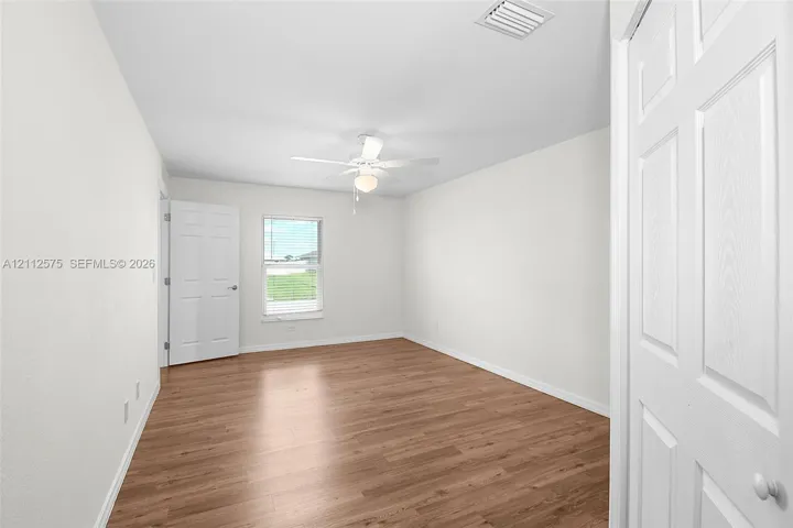 Room featuring wood-finish flooring, a white ceiling fan with integrated light, a single-hung window, and white six-panel interior doors