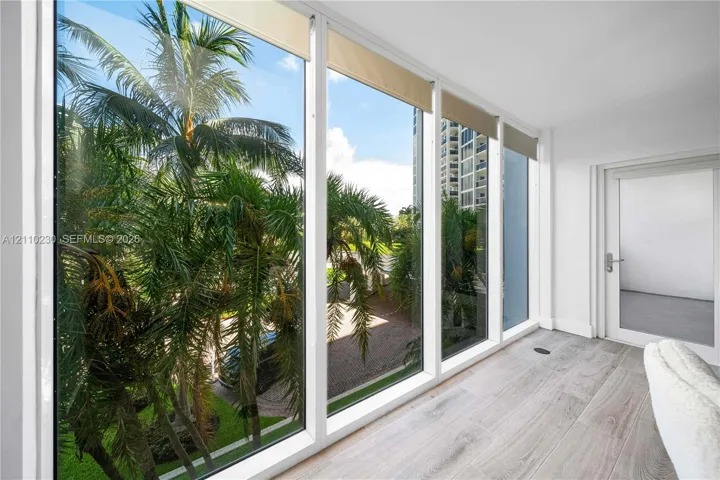 Floor-to-ceiling windows, wood-finish flooring, and single-panel glass door with metallic hardware