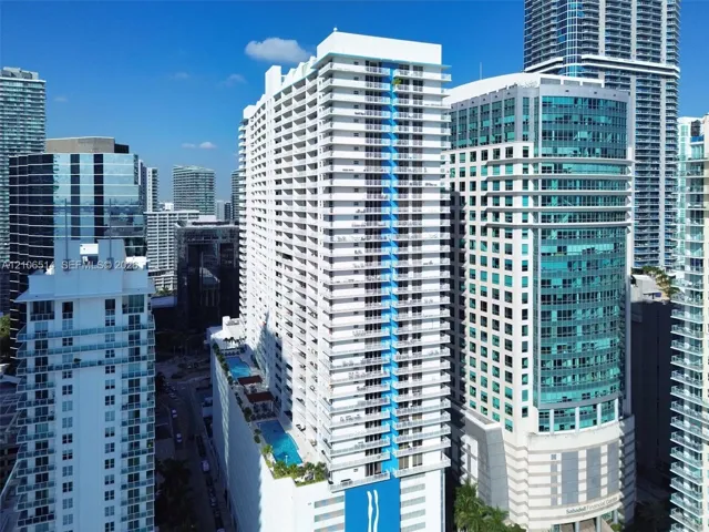 High-rise residential tower featuring multiple levels of private balconies, a multi-tier podium pool deck, and a distinctive blue architectural facade element