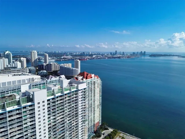 High-rise residential exterior with glass-railing balconies, featuring expansive water and urban skyline scenery