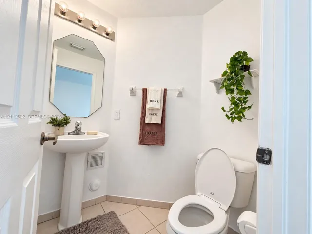 Pedestal sink with chrome faucet, octagonal wall mirror, four-bulb vanity lighting fixture, tile flooring, and wall-mounted shelving