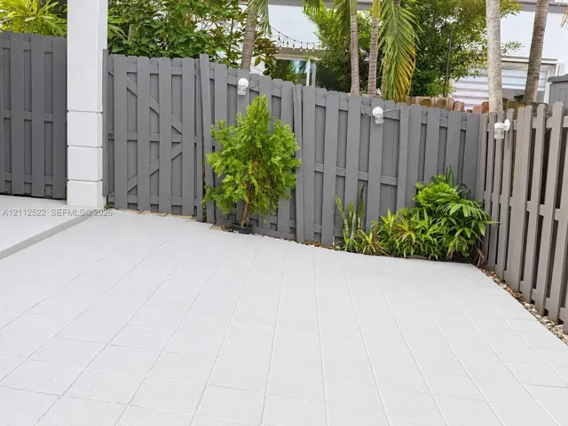 Private rear patio featuring concrete paver flooring, gray privacy fencing, wall-mounted exterior lighting, and integrated landscaping