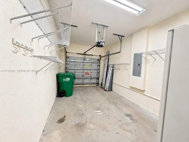 Garage interior featuring concrete flooring, a metal roll-up door, overhead fluorescent lighting, and extensive wall-mounted wire shelving