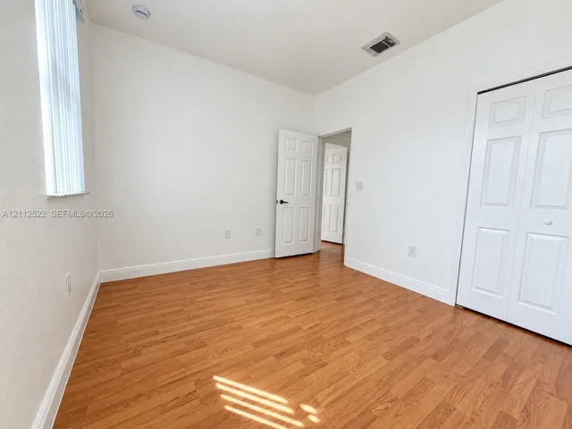 Room featuring wood-finish flooring, white walls, paneled interior doors, and a double-door closet