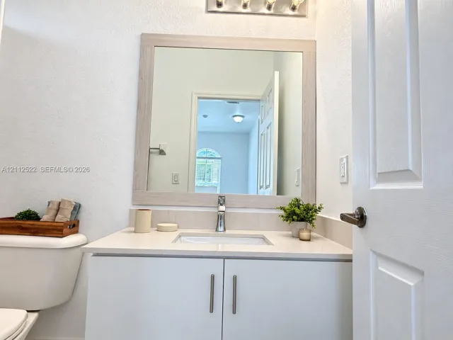 Vanity featuring a light-toned wood-finish frame mirror, stone-composite countertop, undermount sink, and minimalist hardware