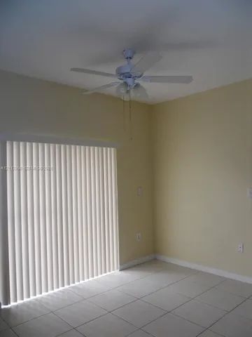 Room featuring ceramic tile flooring, a multi-blade ceiling fan with integrated lighting, and a vertical sliding glass door with blinds