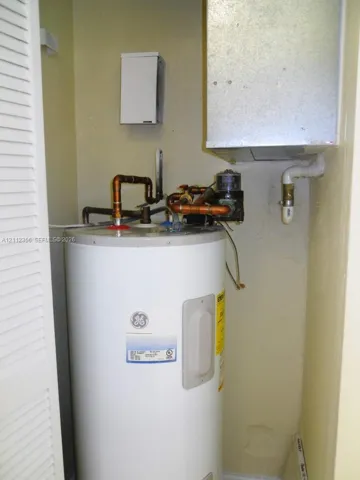 Electric water heater featuring copper plumbing connections, wall-mounted electrical panel, and overhead HVAC ductwork, enclosed by louvered bi-fold doors