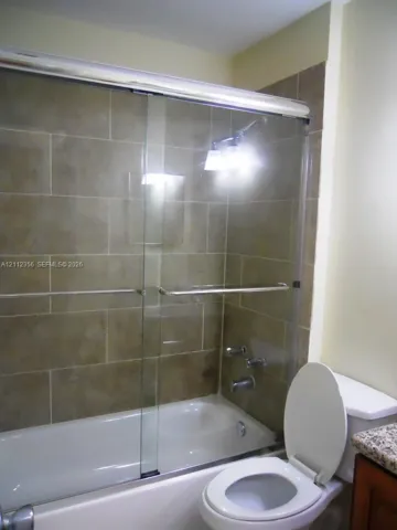 Bathtub featuring a glass sliding door and large-format rectangular wall tile, complemented by a stone-finish countertop
