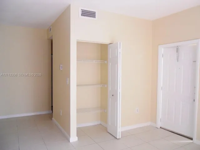 Interior space featuring neutral-toned walls, tile flooring, a six-panel door, and a built-in closet with wire shelving