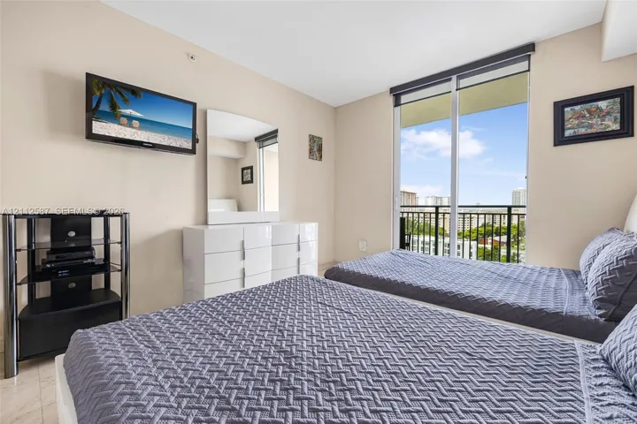 Floor-to-ceiling sliding glass door, private exterior balcony with metal railing, and neutral stone-finish flooring