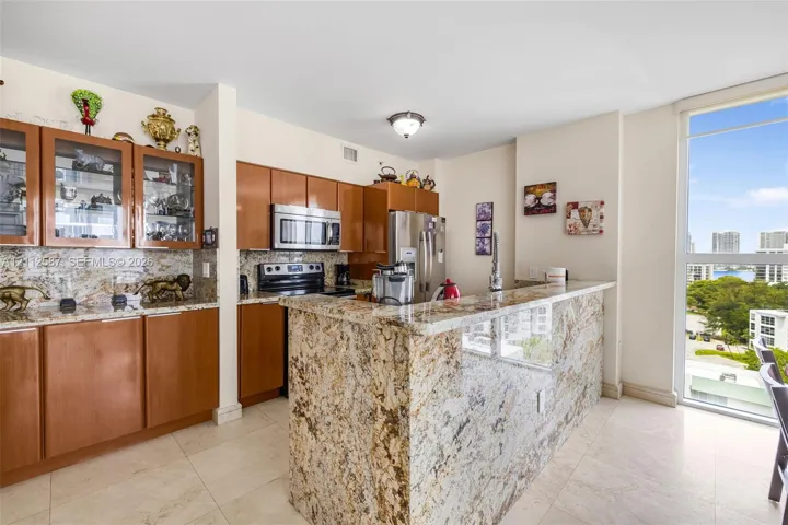 Kitchen featuring wood cabinetry, stone countertops, stone-finish backsplash, stainless steel appliances, and floor-to-ceiling windows