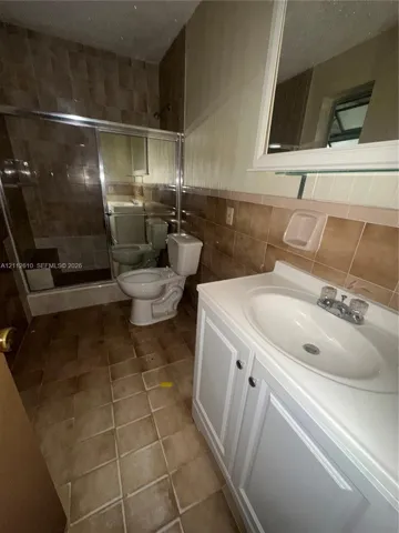 Bathroom featuring a white vanity cabinet with an integrated sink, shower enclosure with tiled walls, ceramic floor tiling, and a wall-mounted mirror
