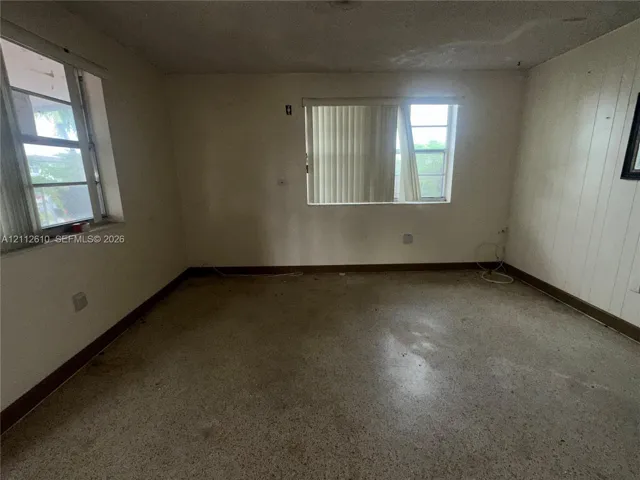 Interior space featuring terrazzo flooring, paneling on one wall, and two windows with horizontal blinds