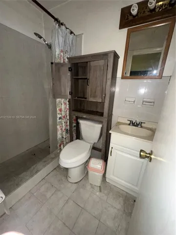 Bathroom featuring a walk-in shower with tiled surround, a vanity with a drop-in sink, a wall-mounted mirror, and tile flooring