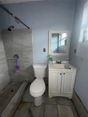 Bathroom featuring a tiled shower enclosure, a white vanity with an integrated sink, a wall-mounted mirror, and tile flooring
