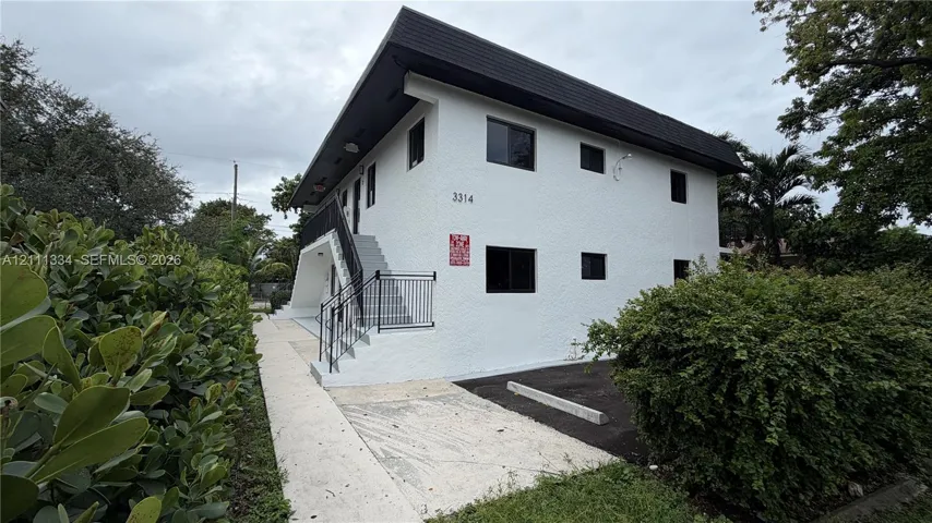 Two-story exterior featuring white stucco siding, a flat roofline, black metal handrails, and surface-level parking