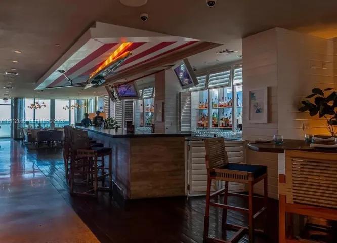 Custom bar featuring dark wood-finish flooring, built-in shelving with integrated lighting, wood-paneled counter, and louvered shutters