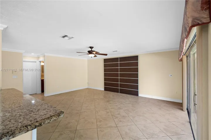 Open-concept interior featuring large-format tile flooring, a stone-surfaced peninsula, a ceiling fan with integrated lighting, and custom dark-toned built-in cabinetry with horizontal detailing