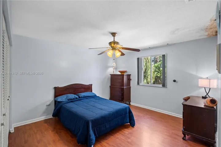 Room featuring wood-finish flooring, a ceiling fan with integrated lighting, and a window with exterior greenery