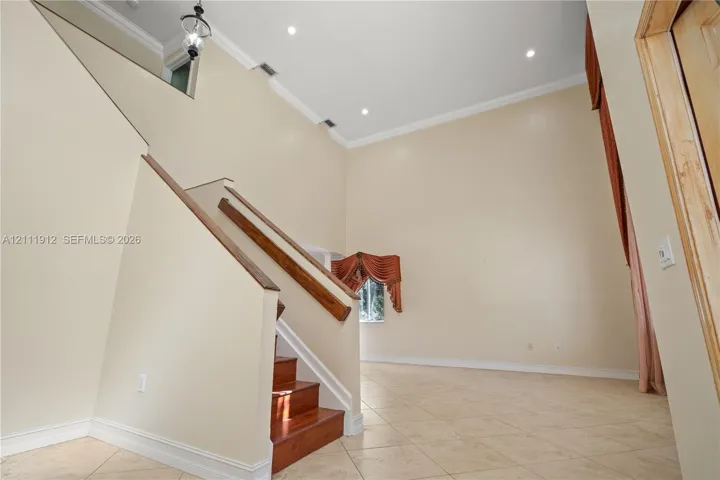 Double-height ceiling, staircase with wood handrail, recessed lighting, and tile flooring