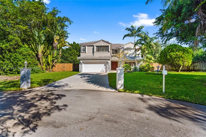 Two-story residence featuring a tile roof, multi-pane windows, attached two-car garage, concrete driveway, and mature landscaping