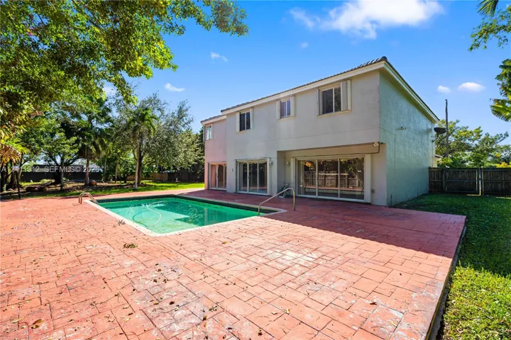 Two-story residence featuring an in-ground swimming pool, expansive stamped concrete patio, sliding glass doors, and mature landscaping