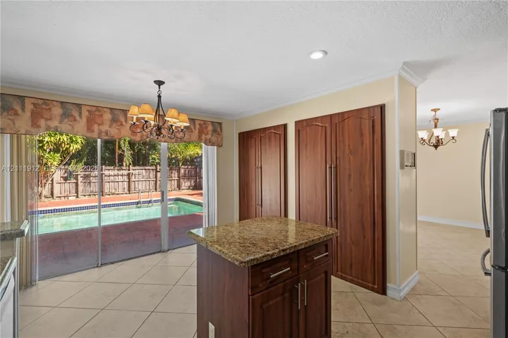 Kitchen featuring a center island with a natural stone countertop, full-height wood cabinetry, neutral tile flooring, and sliding glass doors opening to an exterior swimming pool