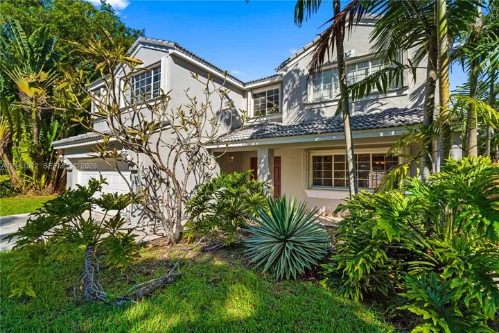 Two-story residence featuring a multi-gabled roofline, light-toned stucco exterior, multi-pane windows, and a paved driveway leading to a multi-car garage