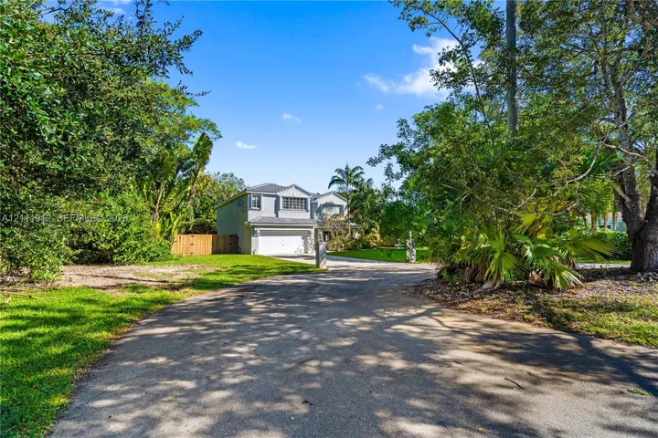 Two-story residence featuring a multi-gabled roofline, an attached two-car garage, an asphalt driveway, and mature landscaping