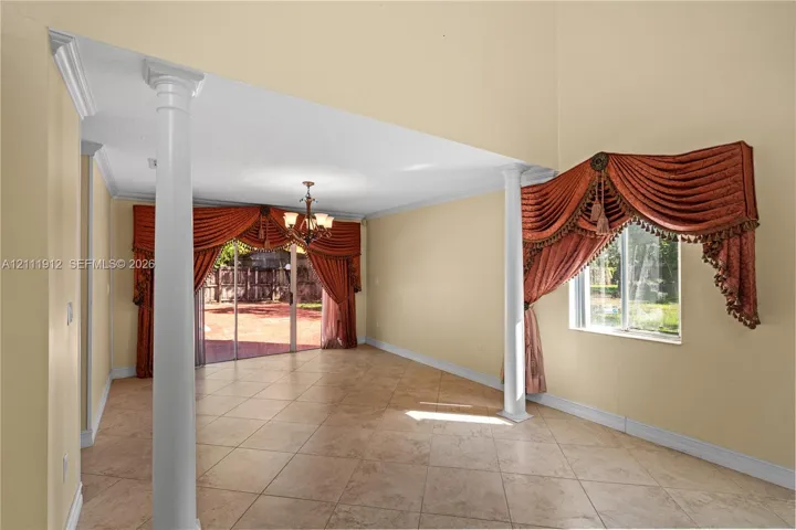 Interior space featuring high ceilings, large-format tile flooring, decorative architectural columns, and sliding glass doors