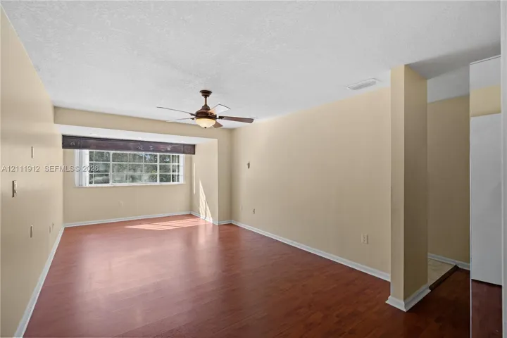 Spacious room featuring wood-finish flooring, a multi-pane window with a valance, and an integrated ceiling fan with a light fixture