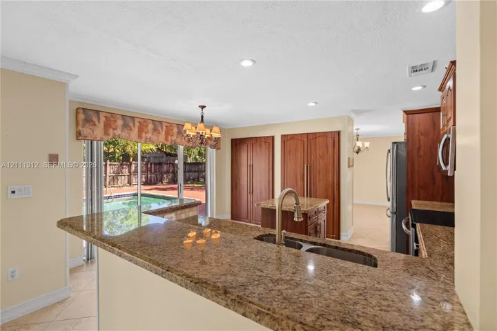 Kitchen featuring a wrap-around stone countertop, recessed lighting, built-in wooden cabinetry, stainless steel sink with gooseneck faucet, and sliding glass doors
