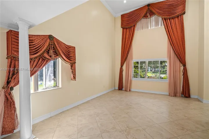 Vaulted ceilings featuring expansive windows, neutral tile flooring, and a decorative column