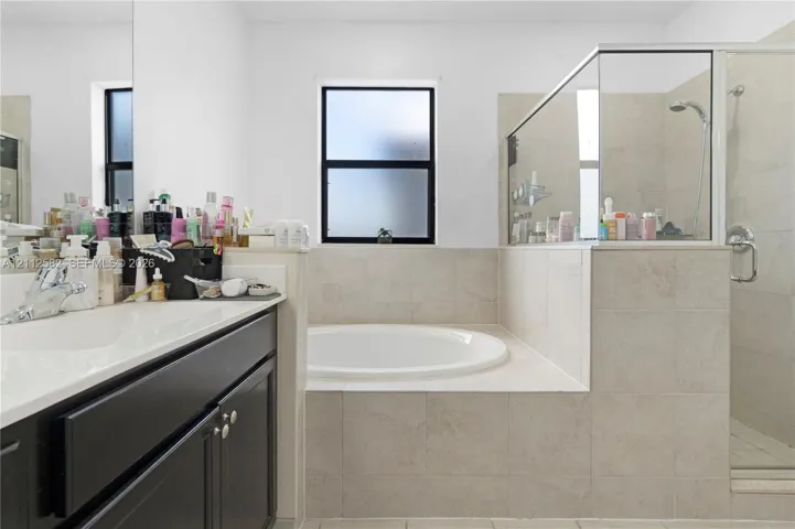 Bathroom featuring a dark wood-finish vanity, solid-surface countertop with an integrated basin, a large soaking tub, and a walk-in shower with tile surround and glass enclosure