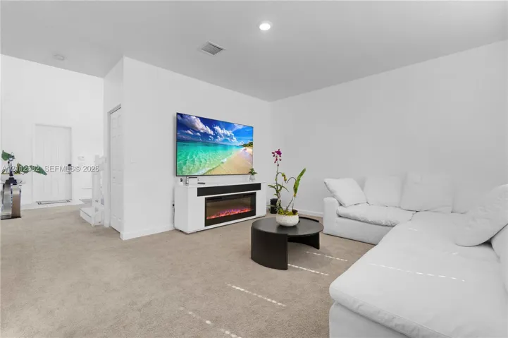 Living area featuring neutral carpeting, recessed ceiling lighting, and a built-in media console with an integrated electric fireplace