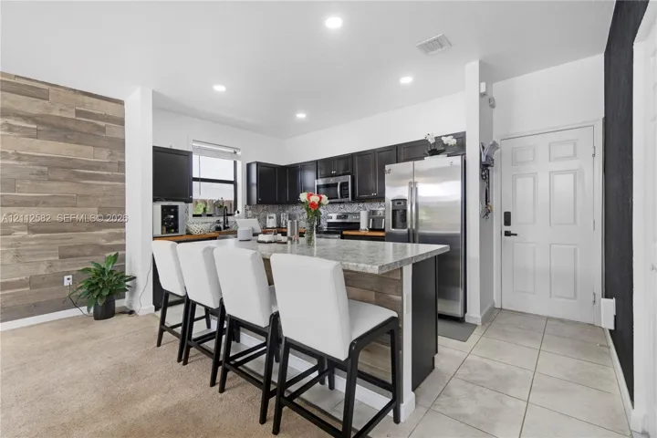 Kitchen featuring a stone-composite countertop island, dark cabinetry, recessed lighting, and a wood-finish accent wall
