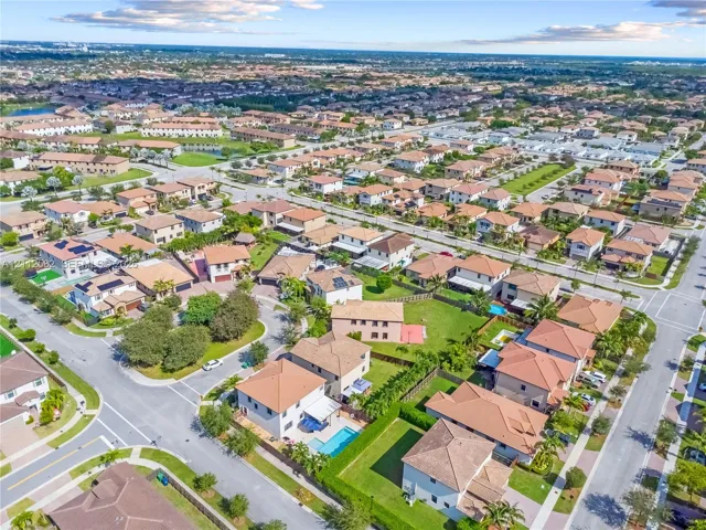 Aerial perspective of a suburban neighborhood featuring paved street infrastructure, multi-level residential homes with tiled roofs, private swimming pools, and manicured landscaping