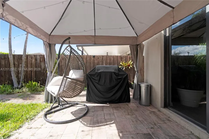 Rear patio featuring paved stone flooring, a fabric-topped gazebo, and a perimeter wood-plank privacy fence
