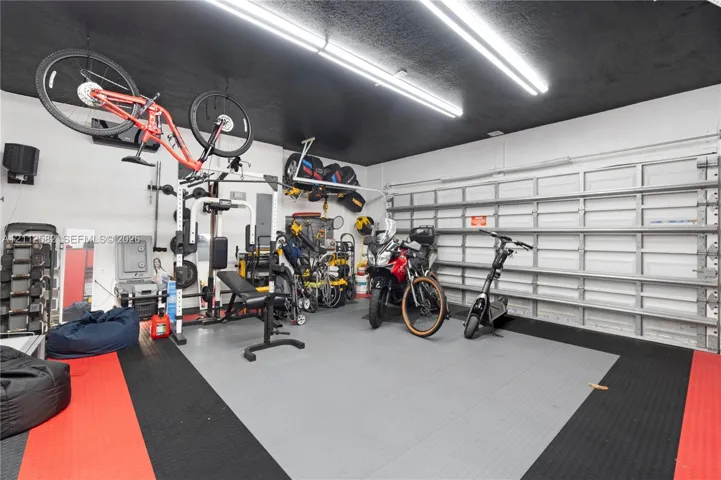 Garage space featuring modular interlocking floor tiles, dual overhead LED tube lighting, and a metal roll-up garage door