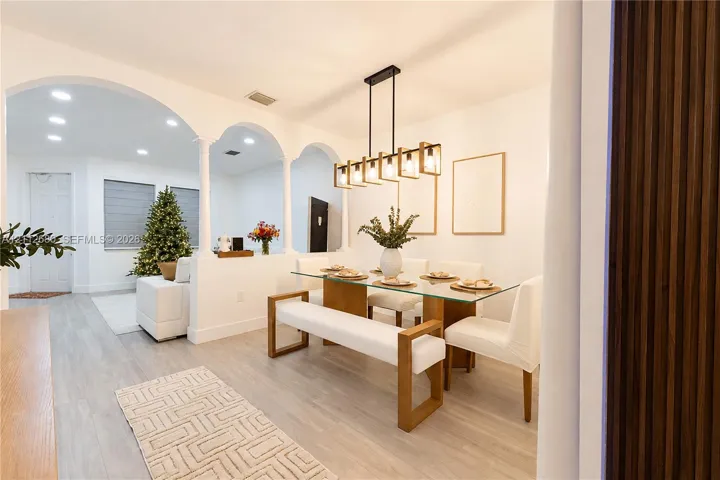 Dining area featuring arched wall openings supported by columns, wood-finish flooring, a linear multi-light metal chandelier, and a vertical wood slat wall accent